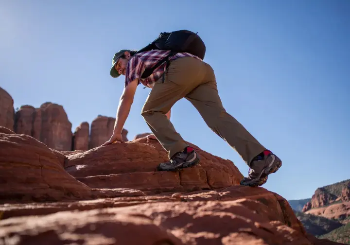 A male hiker expertly scrambles up a steep red rock formation in Sedona, showcasing advanced skills for the dedicated senderista on hiking trails.