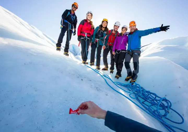 Diverse hikers follow a guide on Matanuska Glacier, with one picking up litter, illustrating Leave No Trace principles and safety on the ice.
