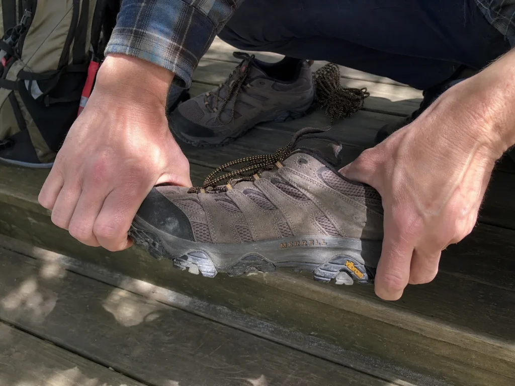 Hands twisting a hiking shoe to test torsional rigidity before a backpacking trip