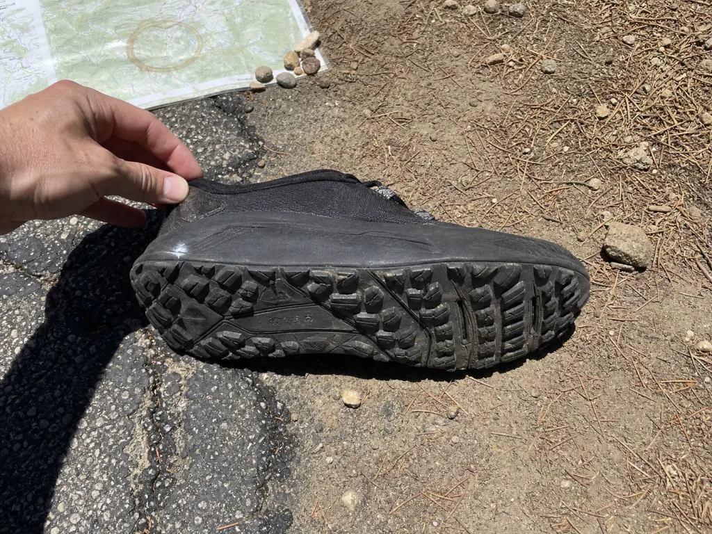 Walking sneaker sole showing shallow road lugs where pavement meets a dirt trail