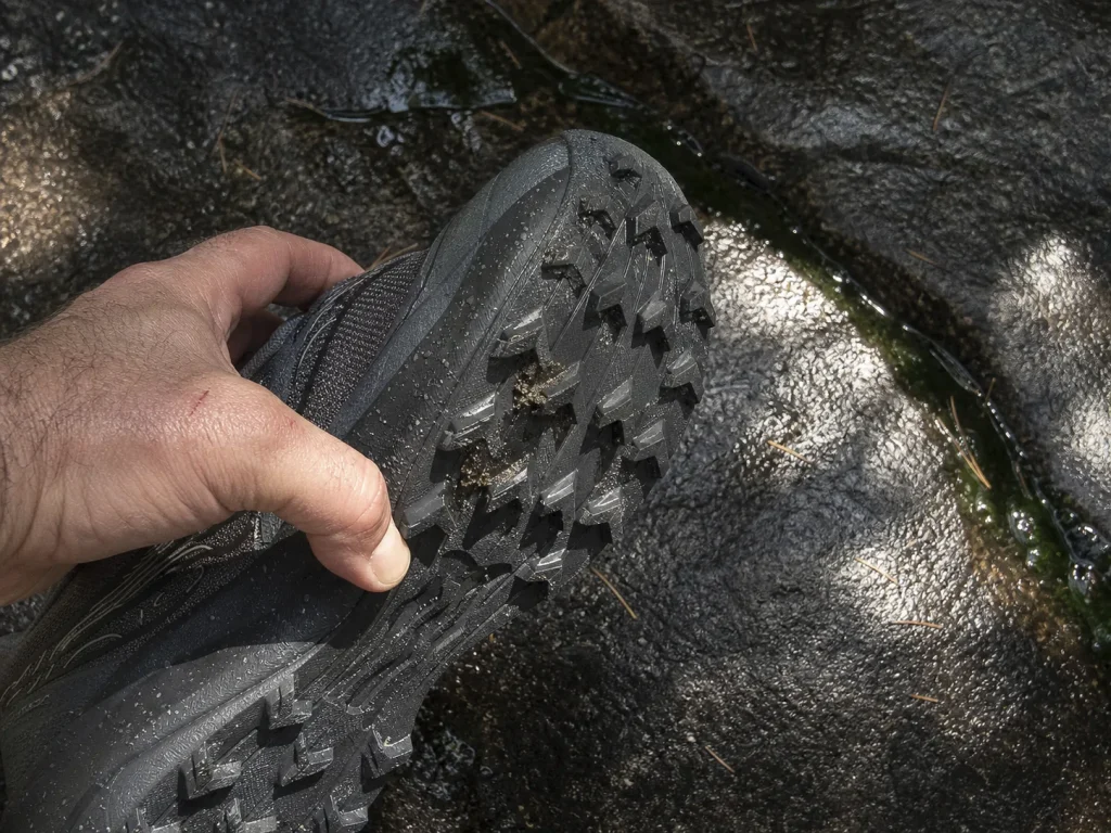 Close-up of deep trail lugs on a Saucony Peregrine 16 outsole held against wet rock
