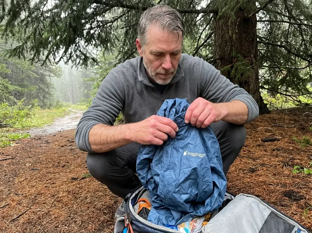 Hiker pulling a Frogg Toggs Ultra-Lite2 emergency rain jacket from the bottom of a pack