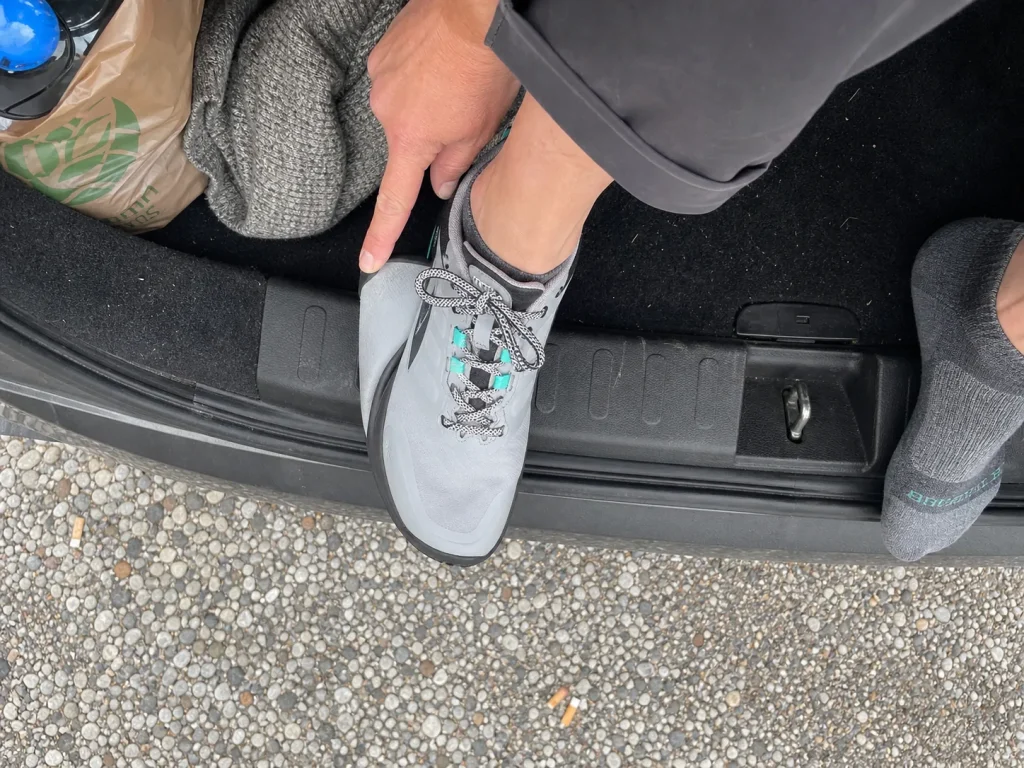 Thumb checking the toe gap in a wide toe box hiking sneaker while seated