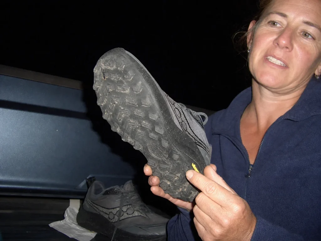 Worn trail sneaker outsole with rounded lugs inspected on a tailgate at dusk