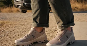 Best Stylish Hiking Shoes That Still Grip the Trail Stylish low-cut hiking shoes on a man's feet where a dirt trail meets a paved sidewalk edge