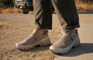 Best Stylish Hiking Shoes That Still Grip the Trail Stylish low-cut hiking shoes on a man's feet where a dirt trail meets a paved sidewalk edge