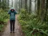 Best Women’s Waterproof Rain Jacket for Your Build Woman in a waterproof rain jacket adjusting her hood on a wet forest trail in steady rain