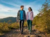 Cool Hiking Shoes 2025: Field-Tested & Stylish Picks A man and woman in a full-body shot, wearing stylish hiking gear, walk along a scenic mountain trail.