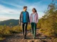 Cool Hiking Shoes 2025: Field-Tested & Stylish Picks A man and woman in a full-body shot, wearing stylish hiking gear, walk along a scenic mountain trail.