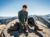 Hiking Socks 2025: Field-Tested Picks & Fit Guide A full-body shot of a hiker in technical gear sitting on a sunny mountain trail, adjusting their hiking boot.