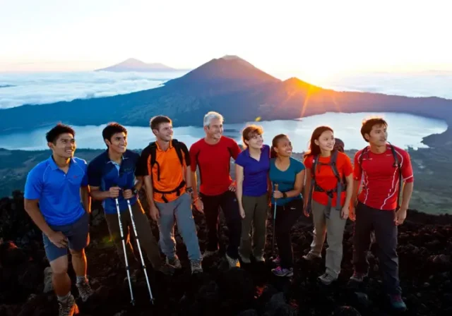 Diverse hikers on the summit of Mount Batur at sunrise, looking at the panoramic view, illustrating key information before booking a Mt. Batur trek.