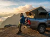 Best Truck Tents for Trailhead Camping (Data-Backed) A hiker in a full-body shot stands next to their pickup truck, which has a truck tent set up in the bed, looking out over a mountain vista at sunrise.
