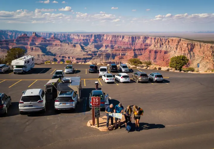 An aerial view of a busy Grand Canyon parking lot with hikers planning their strategy, illustrating the parking puzzle for the Bright Angel Trailhead.