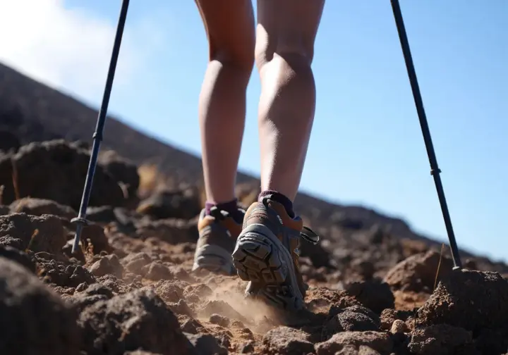 A female hiker with trekking poles navigates loose volcanic scree on Mt. Batur, illustrating the challenging trekking experience from a hiker's perspective.
