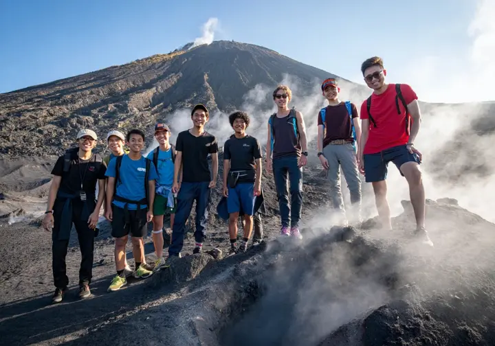 Hikers on Mt. Batur trail with a guide, walking past steam vents on the active volcano, representing safety, risk, and responsibility.