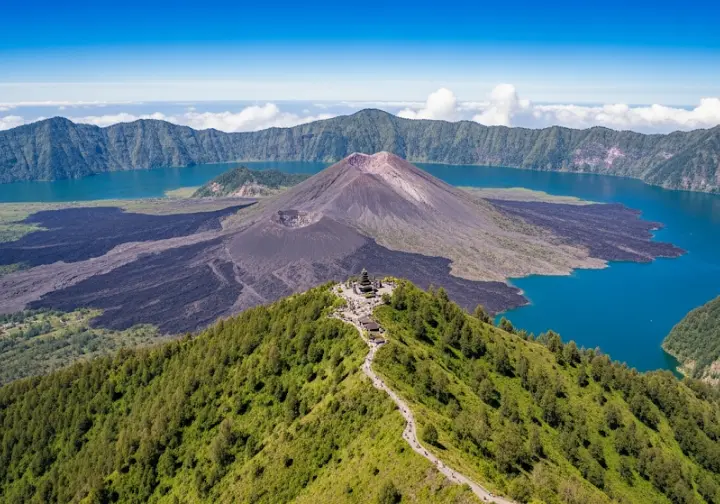 Aerial view of Mount Batur's double caldera system and Lake Batur with a subtle temple on the rim, showcasing its geological and cultural context.