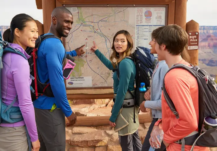 Hikers at a park map kiosk discussing routes and alternatives, representing integrated logistics and transport options for the Bright Angel Trailhead.
