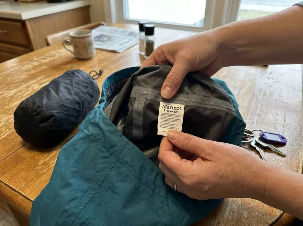 Hands checking the interior spec tag of a waterproof rain jacket before a hike