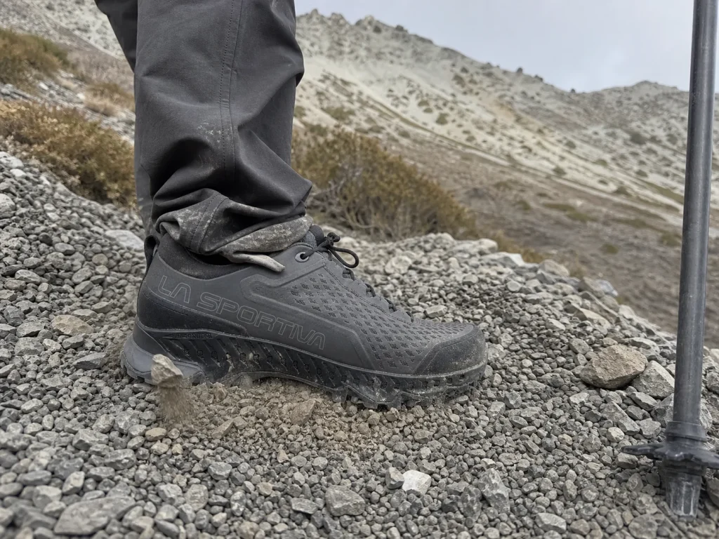 A hiker's sleek low-cut shoe planted on loose rocky scree on a steep trail section