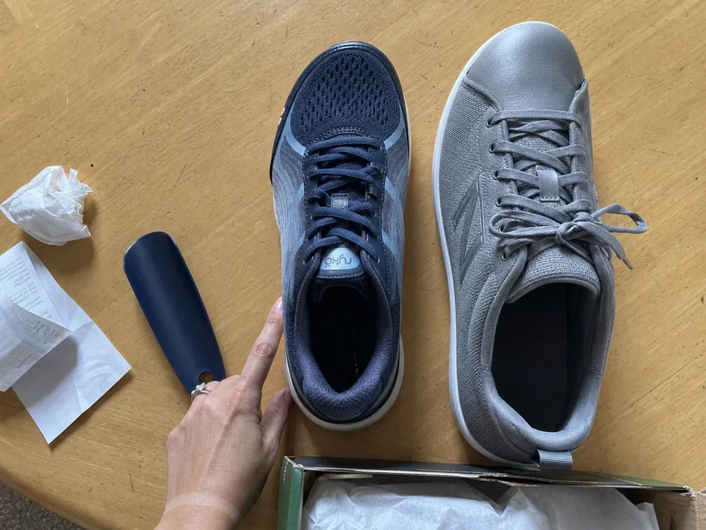 Womens walking shoe next to a mens shoe on a table showing the narrower heel shape