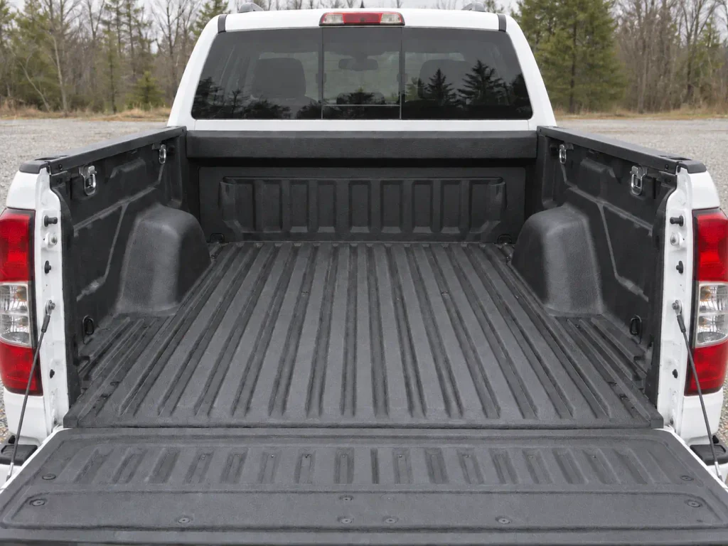 Hands running a tape measure along a pickup bed floor from bulkhead to tailgate