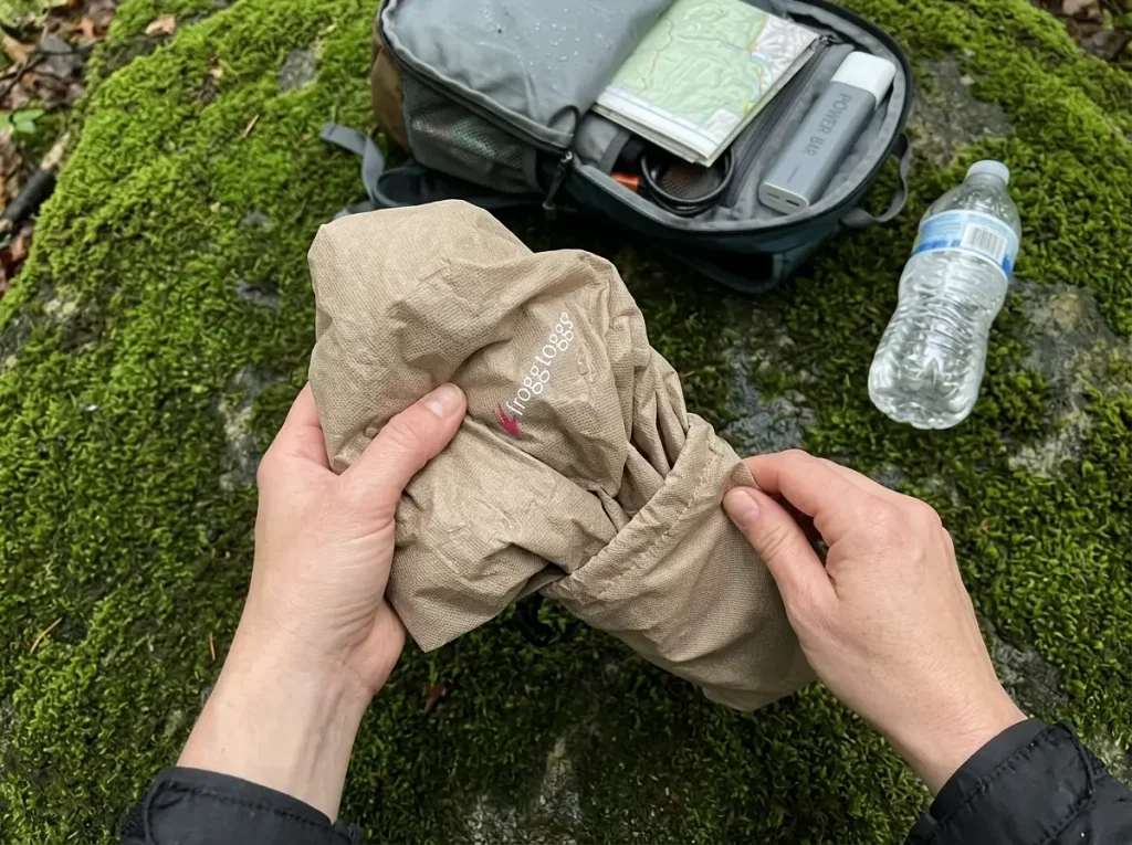 Packing a FROGG TOGGS Ultra-Lite2 budget rain jacket back into its stuff sack on a trailside rock