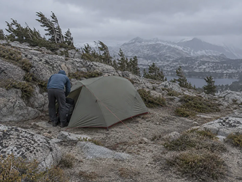Backpacking tent pitched low and fully staked out on an exposed Sierra Nevada bench in wind