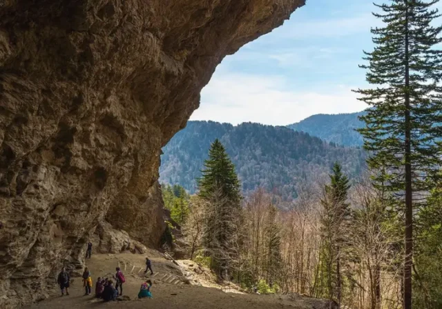 A hiker stands at the base of the towering Alum Cave Bluffs, showcasing the geological feature and the starting point for a hike to Mt. LeConte.