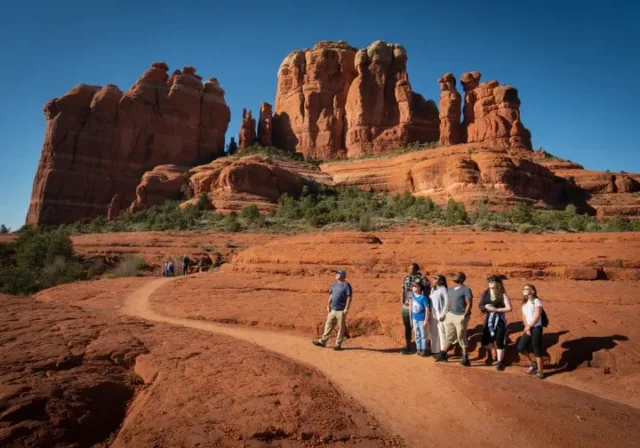 A diverse group of hikers on a trail with Bell Rock and Courthouse Butte in the background, representing the varied experiences and comprehensive guide to hiking Bell Rock.