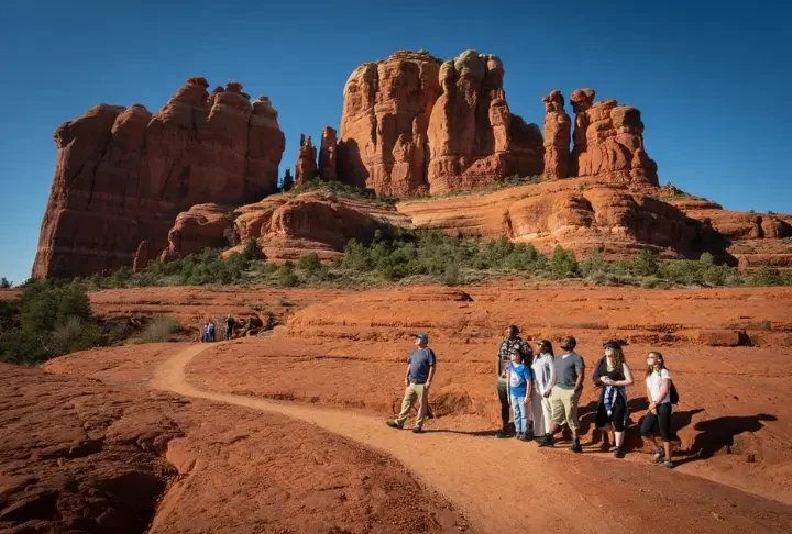 A diverse group of hikers on a trail with Bell Rock and Courthouse Butte in the background, representing the varied experiences and comprehensive guide to hiking Bell Rock.