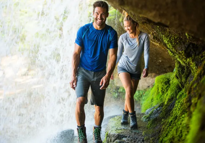 Hikers walk behind Grotto Falls, a unique waterfall in the Smoky Mountains, serving as an excellent alternative to Laurel Falls Trail.