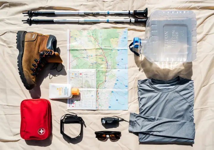 A flat lay display of essential hiking gear for Zion, including a water bottle, map, first-aid kit, and trekking poles, highlighting safety and preparedness.