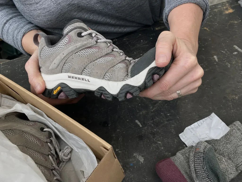 Hands flexing a hiking shoe forefoot to test sole stiffness before buying