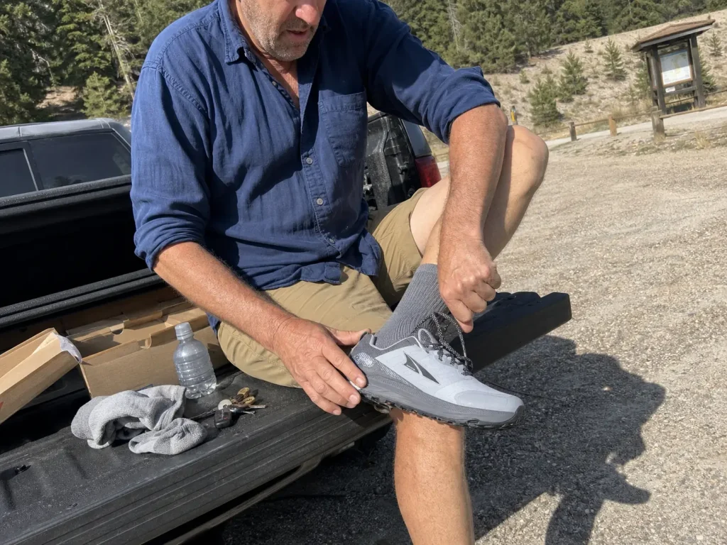 Hiker running the thumb width fit check on a new trekking shoe at a tailgate
