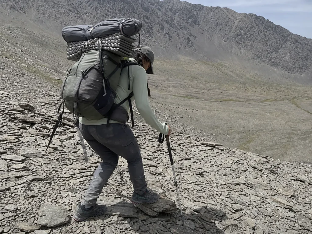 Hiker under a loaded pack stepping across scree in low cut trekking shoes