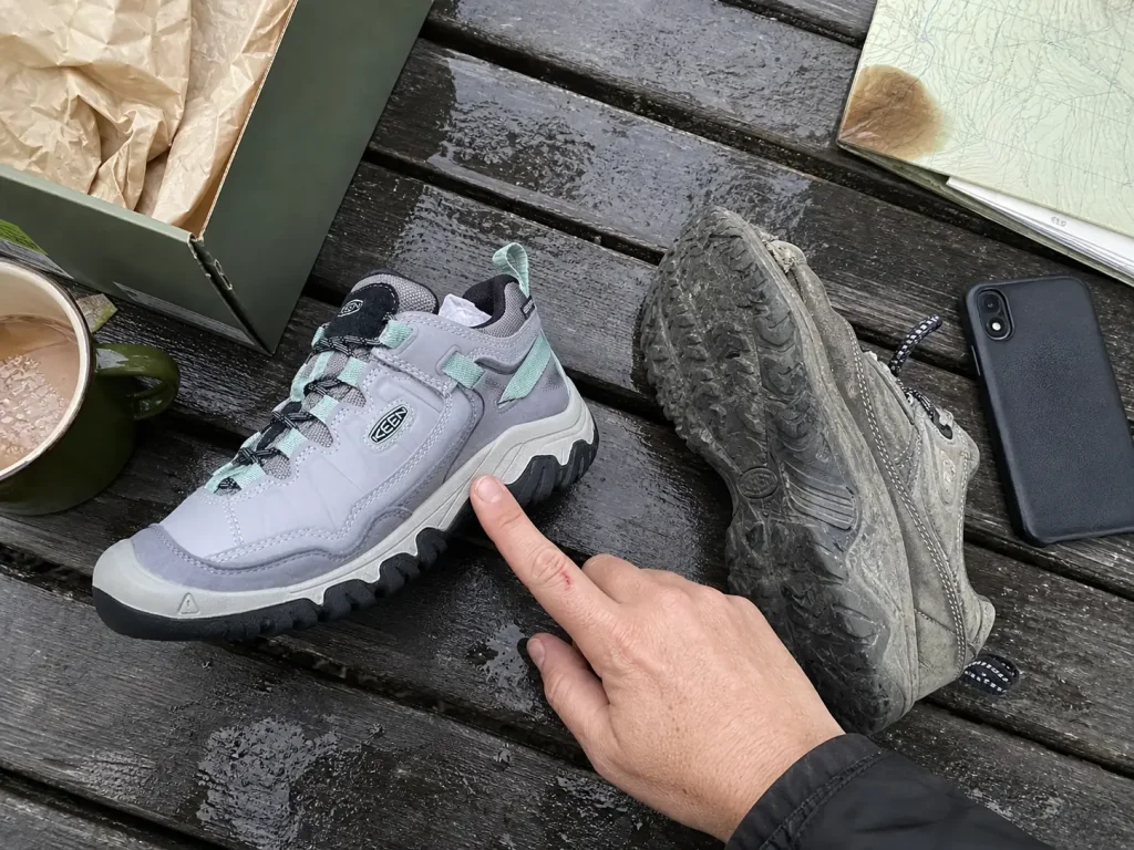 Two trekking shoes side by side on a picnic table while comparing features