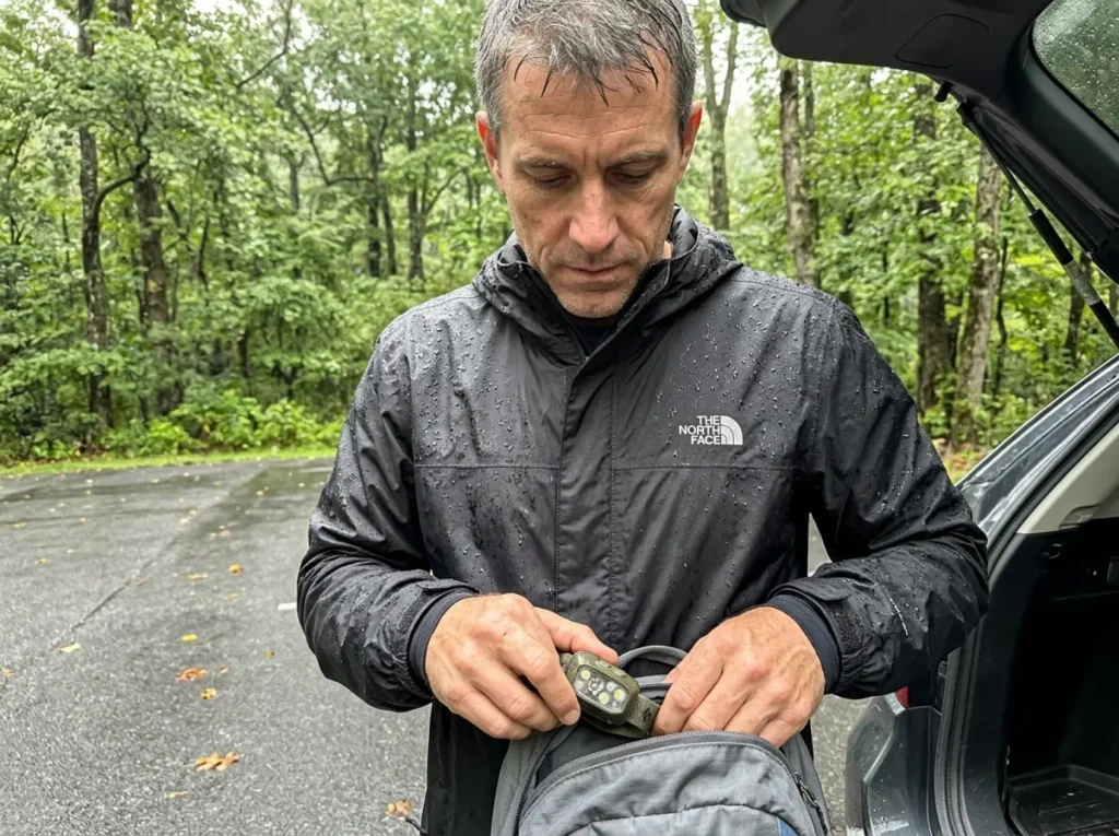Hiker in a North Face Venture 2 rain jacket packing a headlamp before a wet Smokies day hike