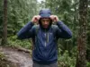 Best Rain Jacket for Hiking That Won’t Wet Out Hiker in an Outdoor Research Helium rain jacket pulling his hood up on a wet trail