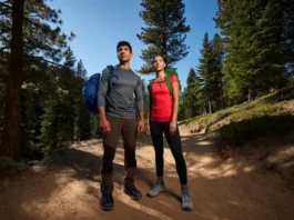 Two diverse hikers stand on a sunlit mountain trail, fully equipped with essential beginner hiking gear, embodying preparedness and confidence.