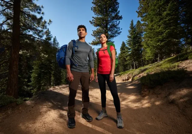 Two diverse hikers stand on a sunlit mountain trail, fully equipped with essential beginner hiking gear, embodying preparedness and confidence.
