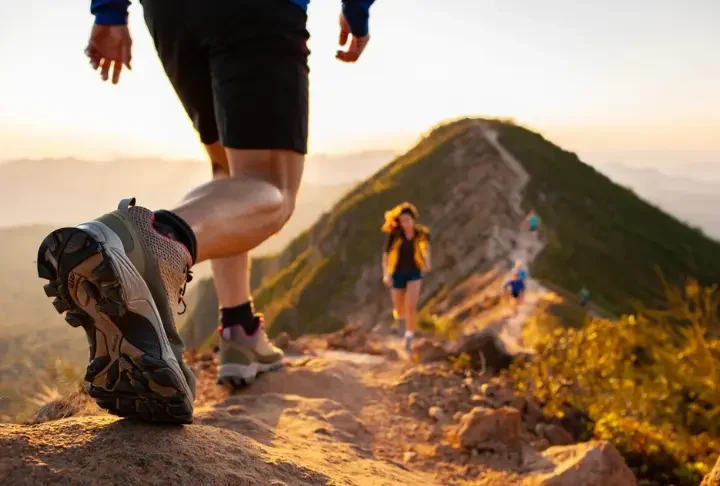 A hiker walks on a mountain trail, showcasing a detailed hiking boot, representing a guide to understanding hiking boot materials, fit, and types.