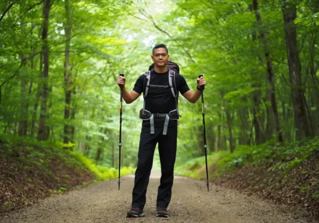 A hiker demonstrates proper hiking pole length for sizing and adjustment on a forest trail.