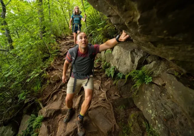 Two diverse hikers navigate a challenging, rocky scramble on the Bear Mountain trail, illustrating the difficulty of the hike.
