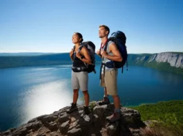 Two hikers stand on a rocky outcrop, gazing at the panoramic view of Minnewaska State Park Preserve, showcasing its diverse trails from lake loops to epic vistas.