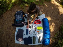A hiker meticulously organizes gear, including a backpack and sleeping bag, laid out in a forest clearing, demonstrating professional backpack packing.
