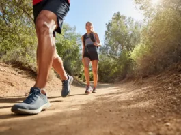 Two hikers on a trail, one in trail runners and the other in hiking shoes, visually representing the choice between different hiking footwear.