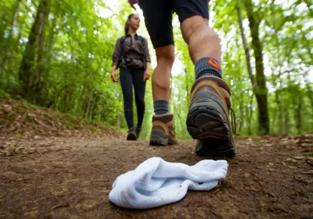 A hiker on a trail, highlighting a proper hiking sock and a discarded cotton sock, representing the ultimate guide to hiking socks.
