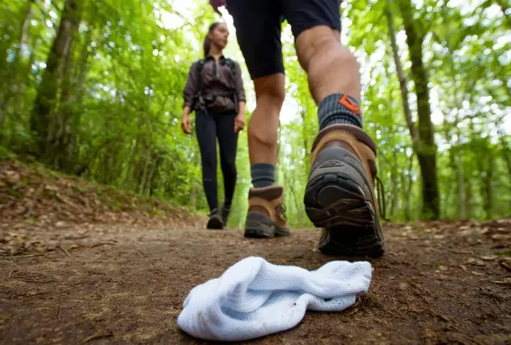 A hiker on a trail, highlighting a proper hiking sock and a discarded cotton sock, representing the ultimate guide to hiking socks.