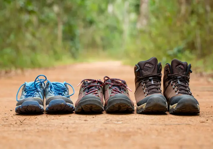A side-by-side comparison of a trail runner, hiking shoe, and hiking boot on a dirt trail, illustrating the spectrum of hiking footwear to choose from.