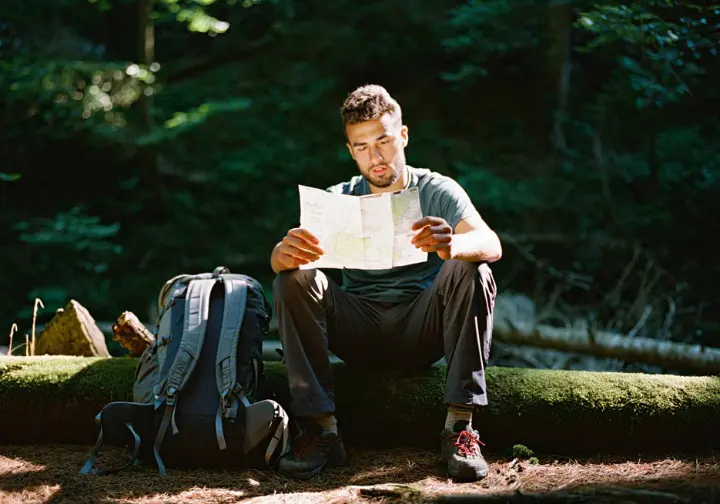 A thru-hiker sits contemplatively in a forest, holding a map, embodying the thoughtful philosophy of packing for a thru-hiking gear list.